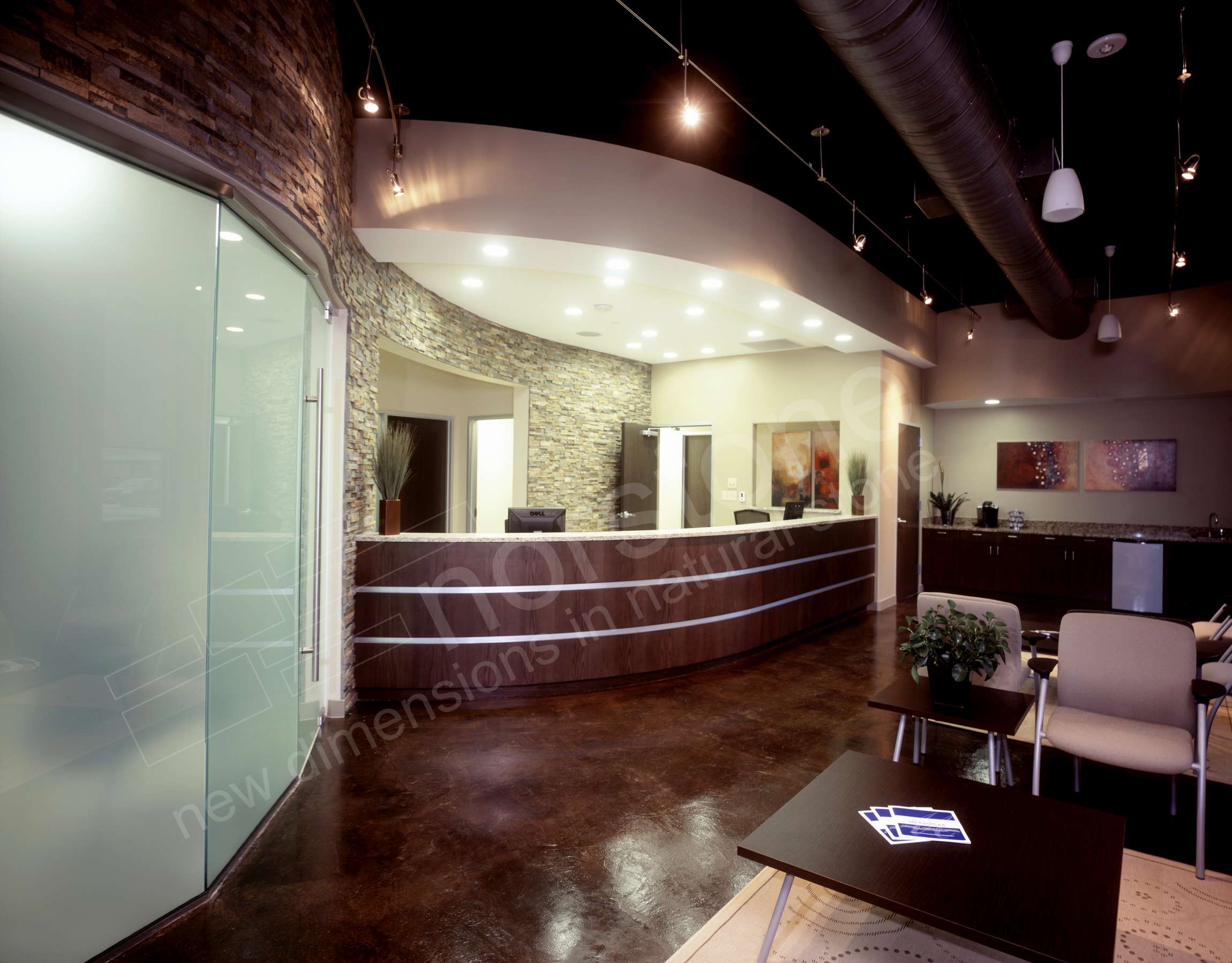 Curved wall starting behind a reception desk and continuing over a large glass doorway in a modern industrial styled medical office.